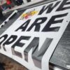 Large black-and-white We Are Open vinyl banner printed by Xenix Graphics
