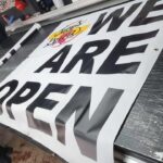 Large black-and-white We Are Open vinyl banner printed by Xenix Graphics